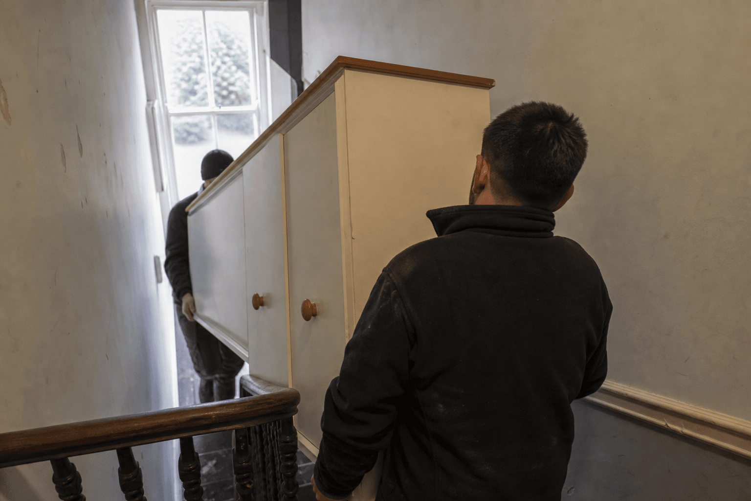Two-man team carrying furniture down stairs on Bedford Hill, Balham