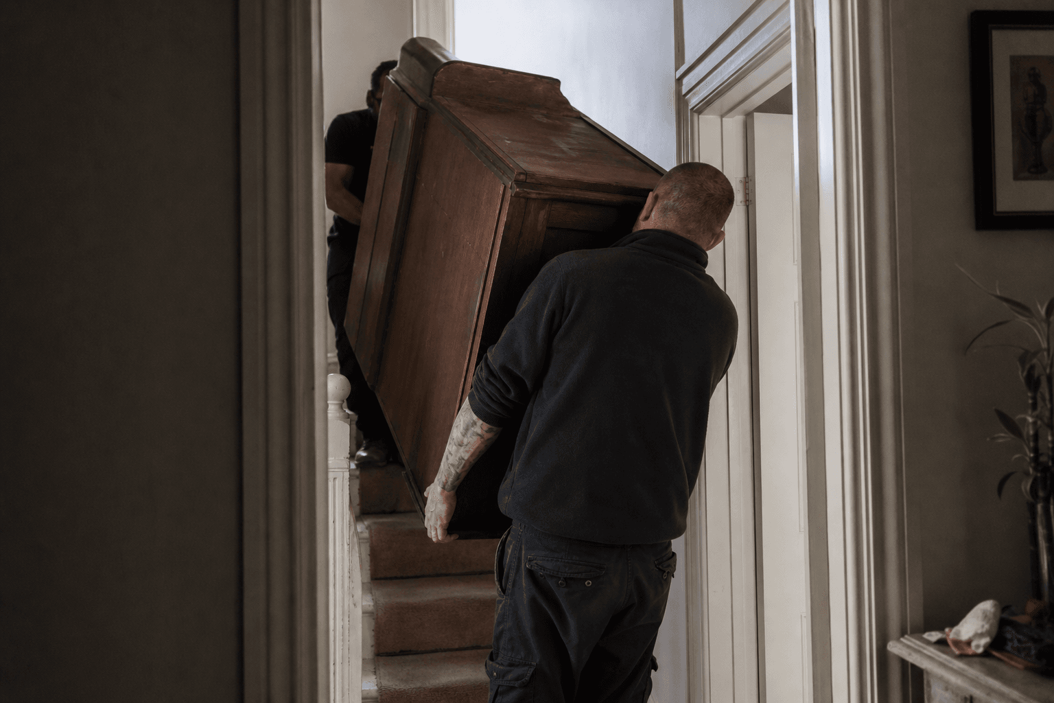 Removal team carrying furniture down narrow stairs in a Clapham Victorian flat