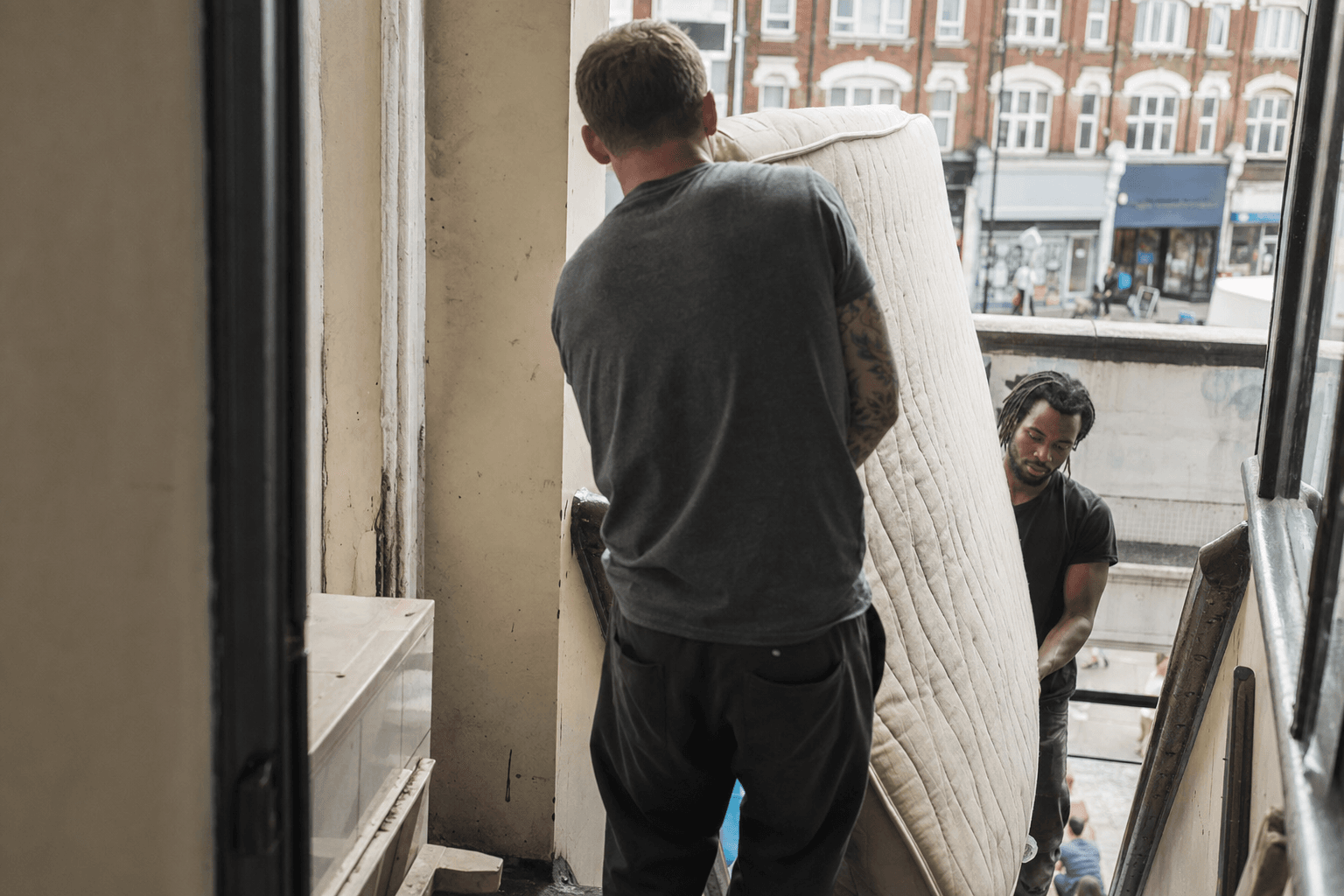 Workers carrying a mattress down stairs from a flat above shops on Tooting High Street