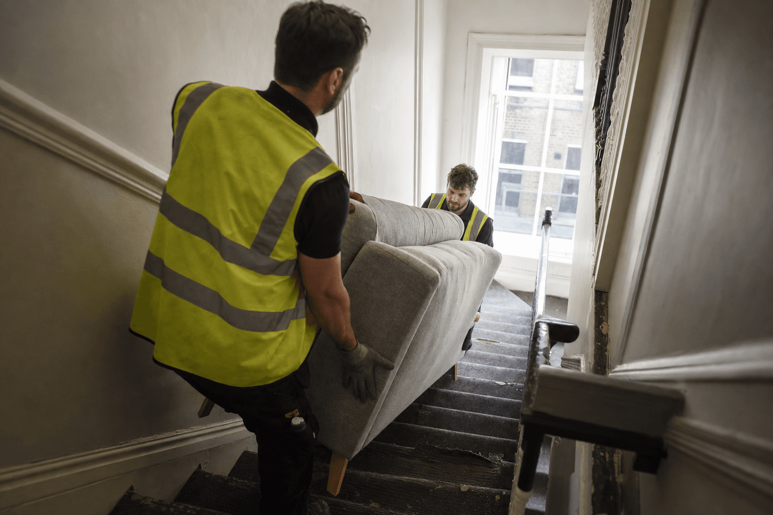 Old sofa removal in London by NV Waste two-man team carrying a sofa out of a flat